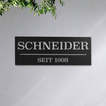 Edelstahl Hausnummernschild personalisiert – Hausschild „SEIT 1998 Schneider“ an der Hauswand, Edelstahl Schwarz RAL 9005 · WesterWerk
