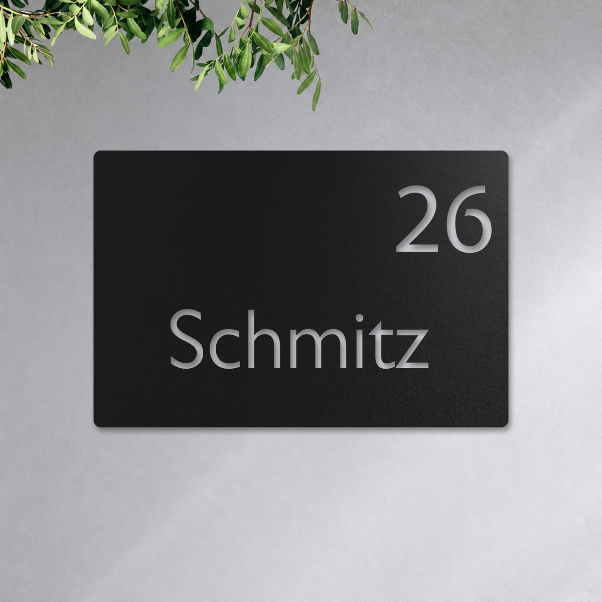 Edelstahl Hausnummernschild personalisiert – Moderne Nummer- und Namensschild „26 Schmitz“ an der Hauswand, Edelstahl Schwarz RAL 9005 · WesterWerk