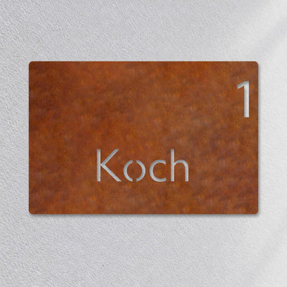 Edelstahl Hausnummernschild personalisiert – Moderne Nummer- und Namensschild „1 Koch“ Nahaufnahme an der Fassade, Edelstahl Cortenstahl · WesterWerk