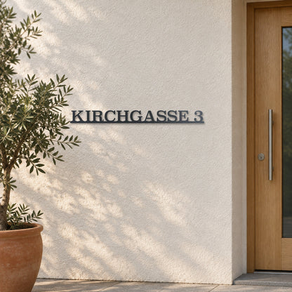 Edelstahl Straßenschild mit Hausnummer personalisiert – Einzeiliges Straßenschild „Kirchgasse 3“ an heller Putzwand, Edelstahl Anthrazit RAL 7016 · WesterWerk