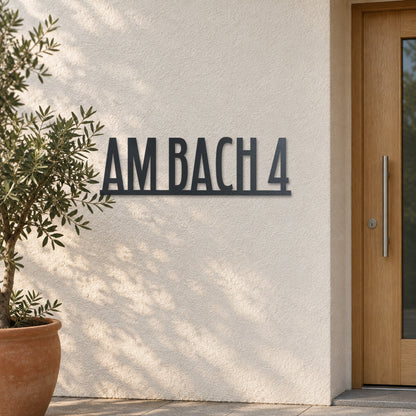 Edelstahl Straßenschild mit Hausnummer personalisiert – Straßenschild Modern „Am Bach 4“ an heller Putzwand, Edelstahl Anthrazit RAL 7016 · WesterWerk
